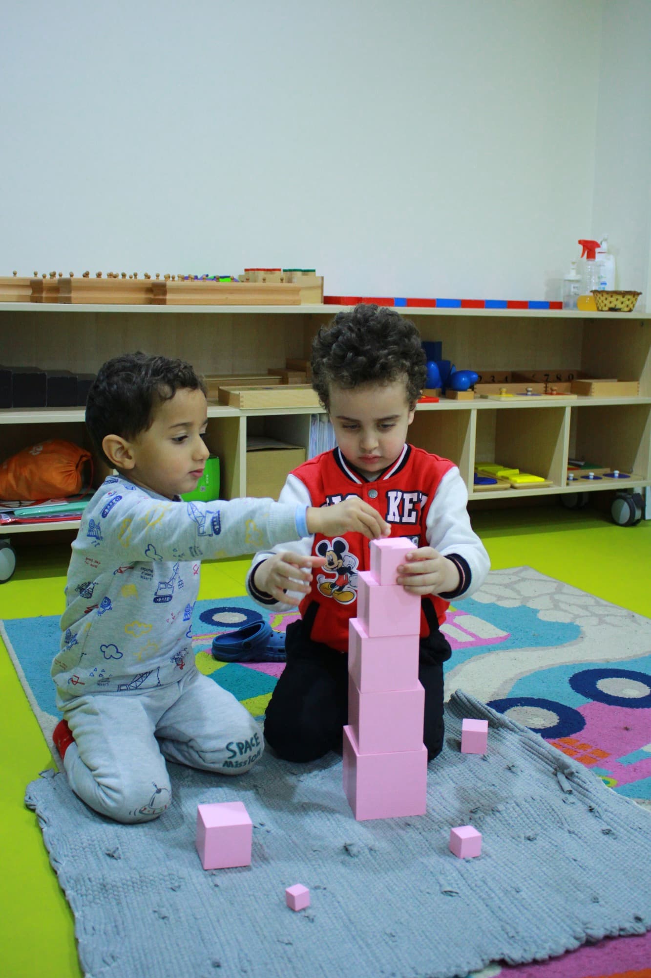 Two children playing together with wooden materials on the rug