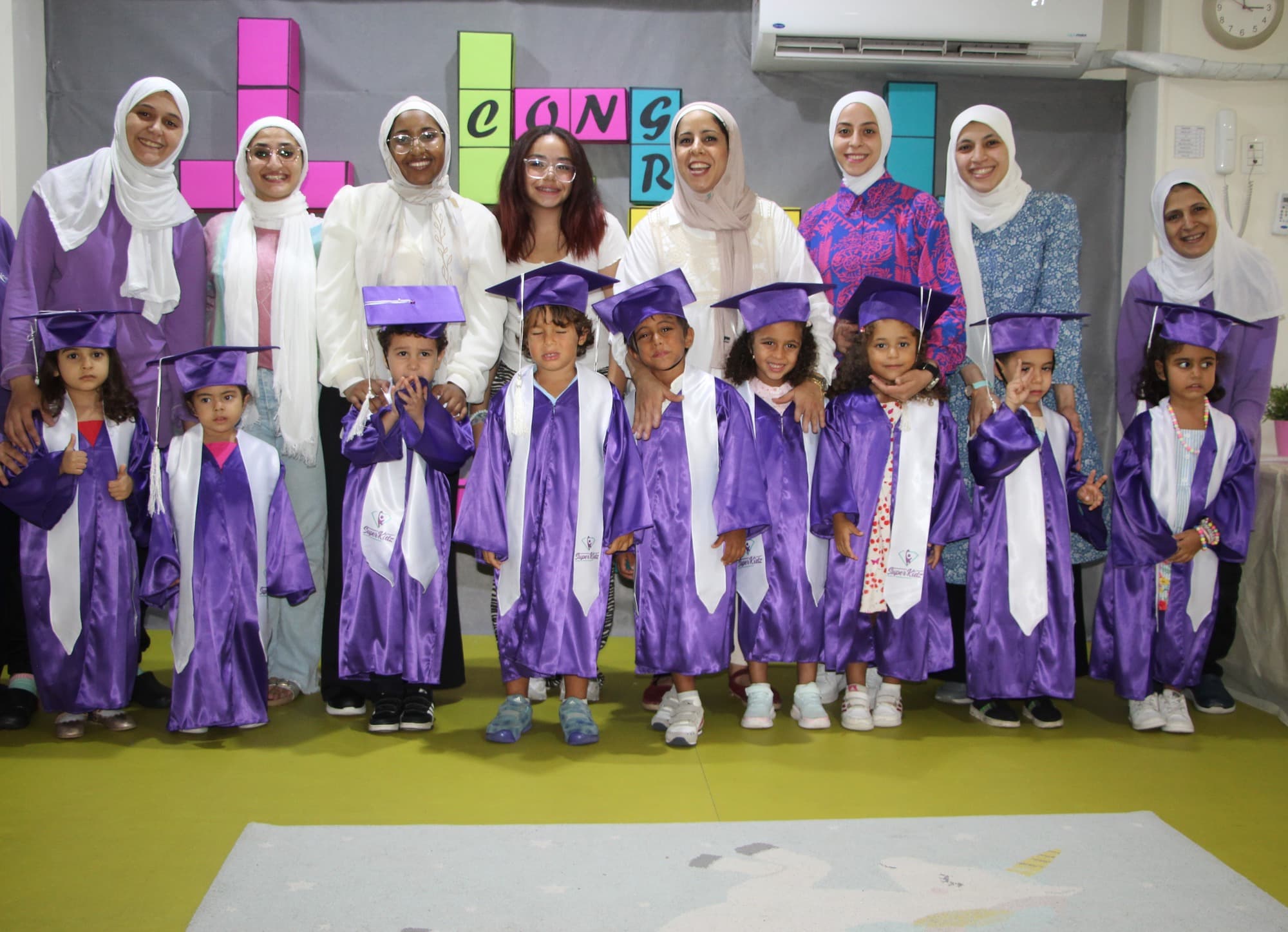 A Super Kidz graduating class posing together in caps and gowns