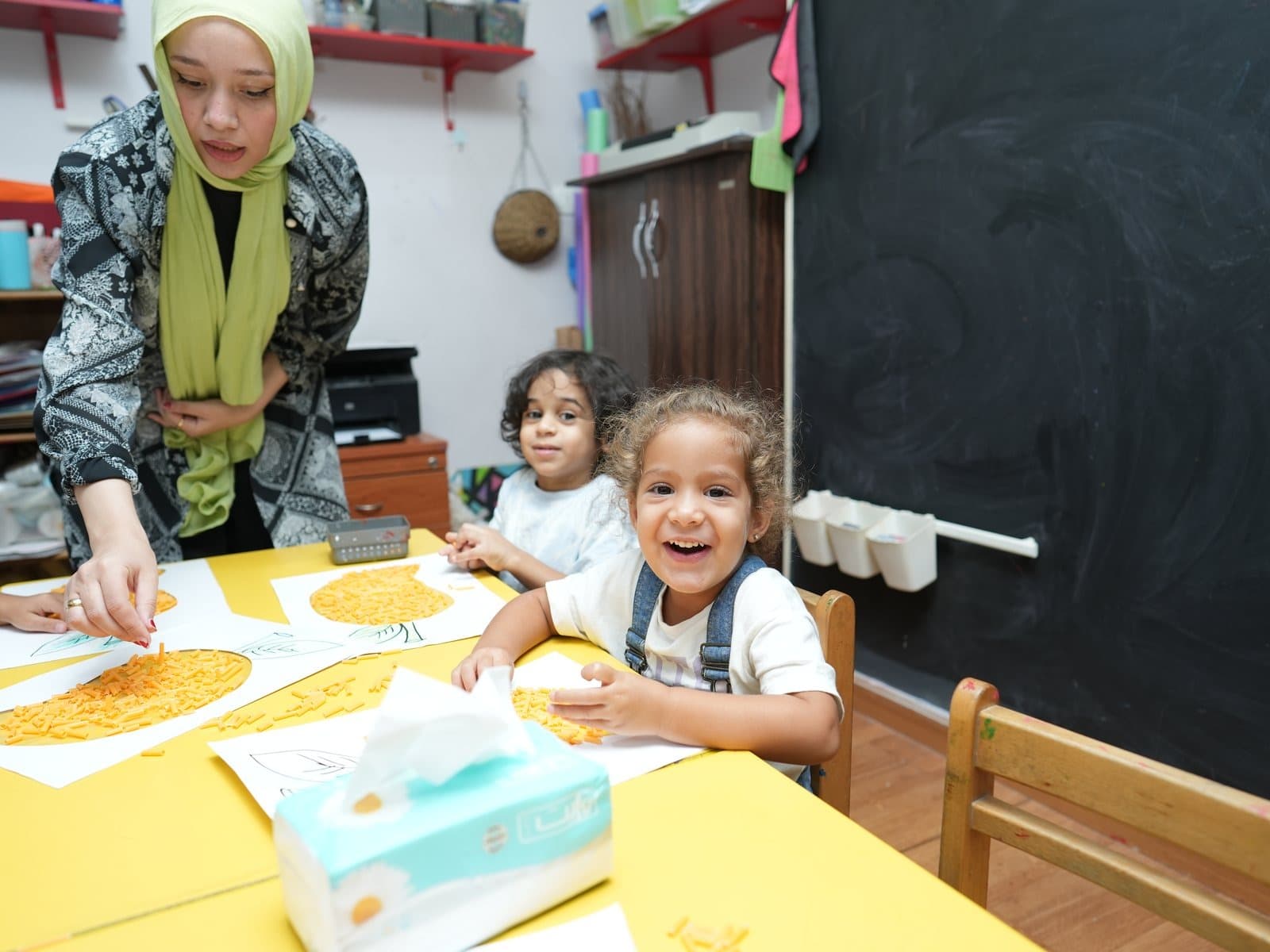 Children painting at the art table with one of the teachers